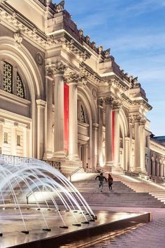 a large building with fountains in front of it and people walking on the sidewalk below