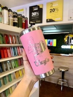 a person holding up a pink tumbler cup in front of a store display case