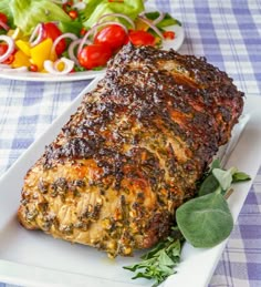 a piece of meat sitting on top of a white plate next to a bowl of salad