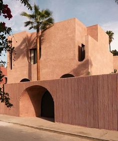 a pink building with palm trees in front of it and a red brick wall on the side