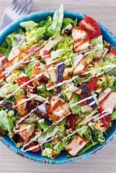 a salad with chicken, lettuce, tomatoes and dressing in a blue bowl