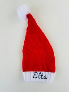 a red and white knitted hat with the word etta written in black on it