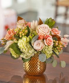 a gold vase filled with flowers on top of a wooden table