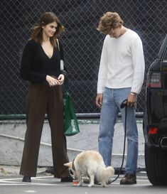 a man and woman are walking their dog in the parking lot while another person holds on to his leash