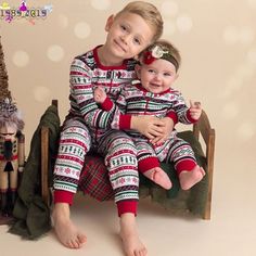 two children in matching pajamas sitting on a chair next to a christmas tree and other holiday decorations