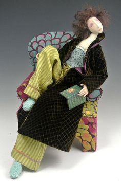 a doll sitting in a chair with a book on it's lap and wearing a robe