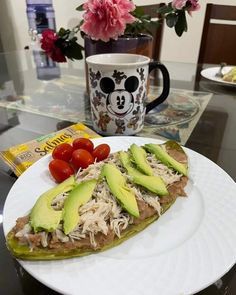 a white plate topped with sliced avocado and tomatoes next to a cup of coffee