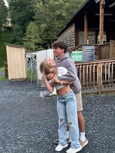 a man and woman hugging each other in front of a wooden structure with trees behind them