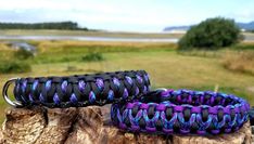 two purple and black paracording bracelets on top of a tree stump in front of a lake