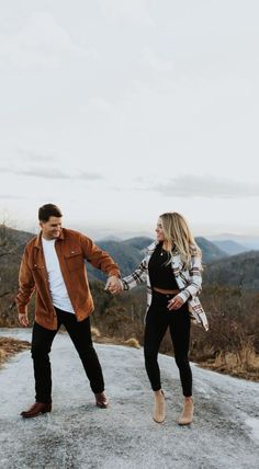 a man and woman holding hands while standing on top of a mountain