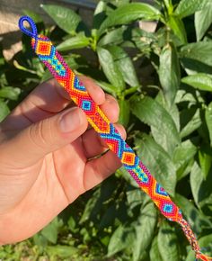 a hand holding a colorful beaded toothbrush holder in front of green plants and shrubbery