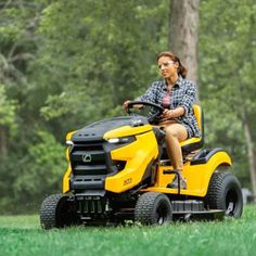 a woman riding on the back of a yellow ride - on mower in a park