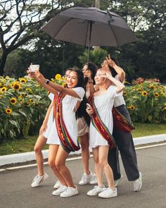 three young women are standing under an umbrella and taking pictures with their cell phones in the street