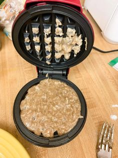 a waffle maker with some food inside of it on a table next to plates and forks