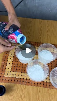 someone is pouring something into four plastic containers on a table with other bowls and cups