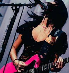 a woman holding a pink guitar in front of a microphone