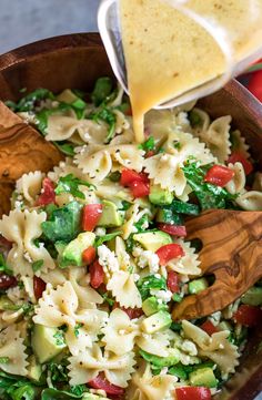 a wooden bowl filled with pasta salad and dressing being drizzled over it