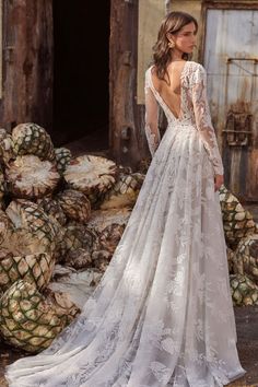 a woman in a wedding dress standing next to piles of pineapples and looking at the back