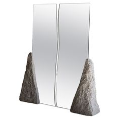 two mirrors are standing next to each other with rocks in front of them and one is reflecting the image