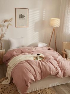 a bed with pink comforter and pillows in a white room next to a lamp