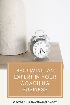 an alarm clock sitting on top of a table next to a vase with the words becoming an expert in your coaching business