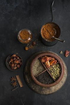 an assortment of spices and seasonings in bowls on a black surface with spoons