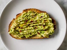 a white plate topped with a piece of bread covered in guacamole