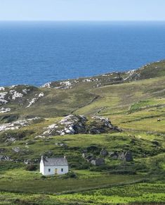 a small white house sitting on top of a lush green hillside next to the ocean