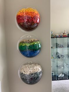 three plastic bowls filled with legos on top of a white wall next to a glass case