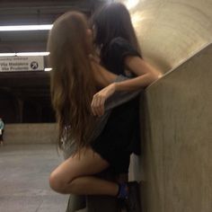 two women are hugging each other in an underground subway station, one is leaning against the wall