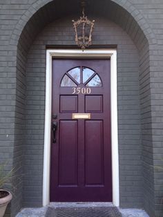 a purple door is in front of a gray brick building with potted plants on either side