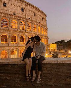 two people are sitting on a brick wall in front of the colossion at night