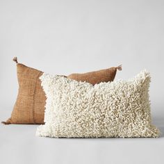 two pillows with tassels on them sitting next to each other in front of a white wall