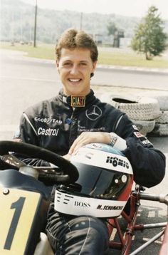 a man sitting on top of a motorcycle next to a race car in a parking lot