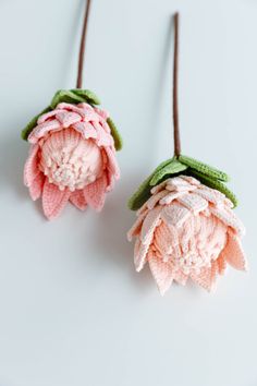 two crocheted flowers are hanging from leather cords on a white surface, one is pink and the other is green