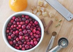 a bowl of cranberries next to scissors and an orange on a table with other items