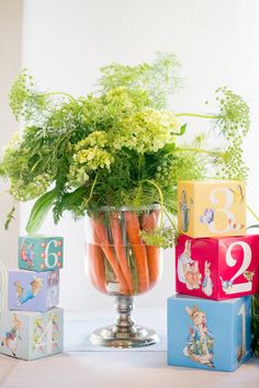 carrots and other vegetables in a glass vase on a table with boxes around it