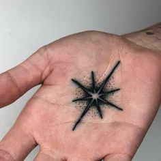 a person's hand with a small black star tattoo on the middle of it