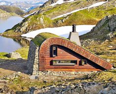 an unusual house built into the side of a mountain with a lake in the background