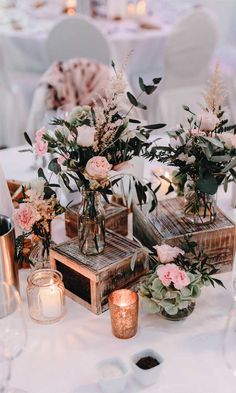 the table is set with vases and flowers on top of wooden crates, which have candles in them