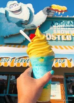 a hand holding an ice cream sundae in front of a toy story store with the sign above it