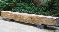 a large wooden bench sitting on top of a cement floor next to bushes and trees