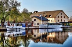 two boats are docked in the water next to some buildings and trees on the other side of the river