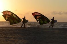 two people carrying kites on the beach at sunset