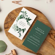 two green and white business cards sitting on top of a wooden tray next to some flowers