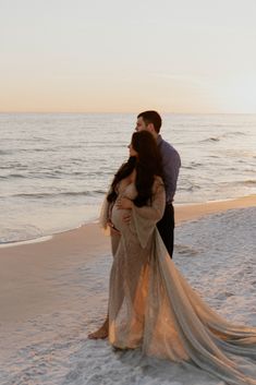 a man and woman standing on top of a beach next to the ocean at sunset