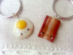 two key chains with eggs and bacon on them sitting next to each other in front of a white towel