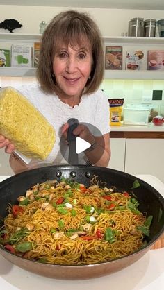 a woman holding a loaf of bread in front of a pan filled with spaghetti and vegetables