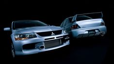 two silver cars parked next to each other in a dark room with their hoods open