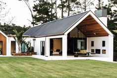 a white house with a black roof in the middle of some trees and green grass